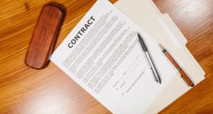 High-angle view of a contract document with pens and a case on a wooden table.
